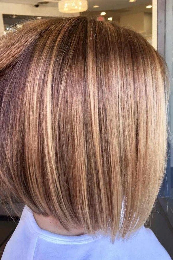 Close-up back view of a person's straight bob haircut with blonde and brunette highlights, indoor lighting.